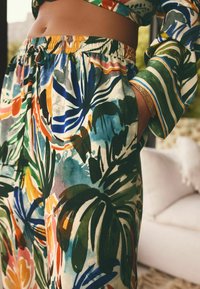 Pantalons avec un imprimé botanique éclatant et multicolore en vert, bleu et orange, dotés d'une taille élastique et de poches latérales.
