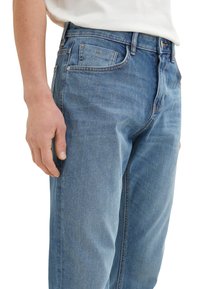 Jeansi din denim bleu deschis cu un design clasic cu cinci buzunare, croială dreaptă și o ușoară decolorare. Textura materialului este netedă și durabilă.