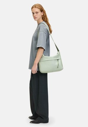 Hellgrüne Leder-Umhängetasche mit schlankem Design, einer mit Reißverschluss versehenen Tasche auf der Vorderseite und einem verstellbaren Trageriemen. Glatte Textur und minimalistisches Format.
