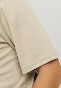 Chemise beige à manches courtes avec un tissu lisse et texturé. L'ourlet est cousu régulièrement, offrant une finition nette au bord des manches.