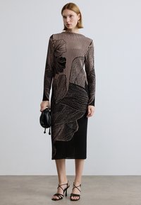 Robe longue ajustée avec un motif noir et beige comprenant des rayures verticales et des dessins floraux. Confectionnée dans un tissu léger texturé.