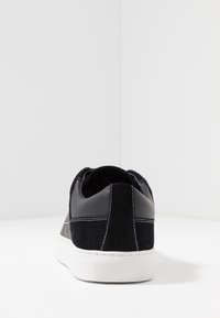 Sneaker nera in suede e pelle con suola in gomma bianca. Presenta cuciture a contrasto e un tallone arrotondato. Vista dal retro, design minimalista.