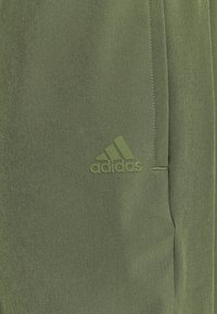Green athletic shorts made of smooth fabric with a subtle texture. Features a small embossed Adidas logo on the front.