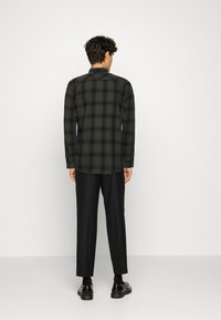 Langouwige geruite overhemd in donkergroen en zwart, met een button-down kraag, gedragen met een zwarte goed passende broek en zwarte schoenen.