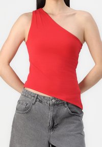 Asymmetrisch rood top van rekbare stof met een schouderontwerp, gecombineerd met hoog waaiers grijze denim shorts.