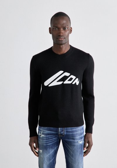 Sort strikket sweater med rund hals og hvidt "ICON" logo i midten. Båret med lyseblå slidte jeans.