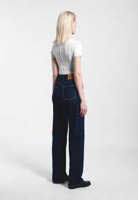 Džíny s vysokým pasem z tmavého denimu s kontrastním prošíváním, které mají na zadní části pasu hnědý kožený štítek, a upnuté bílé tričko s krátkým rukávem.