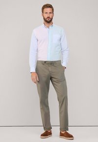 Camicia a maniche lunghe a righe blu chiaro e bianche, abbinata a pantaloni khaki e scarpe in suede marroni. La camicia presenta una tasca sul petto.