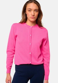 Cardigan rose vif en tissu doux avec un col rond et des boutons sur le devant. Il possède des manches longues et une silhouette ajustée.