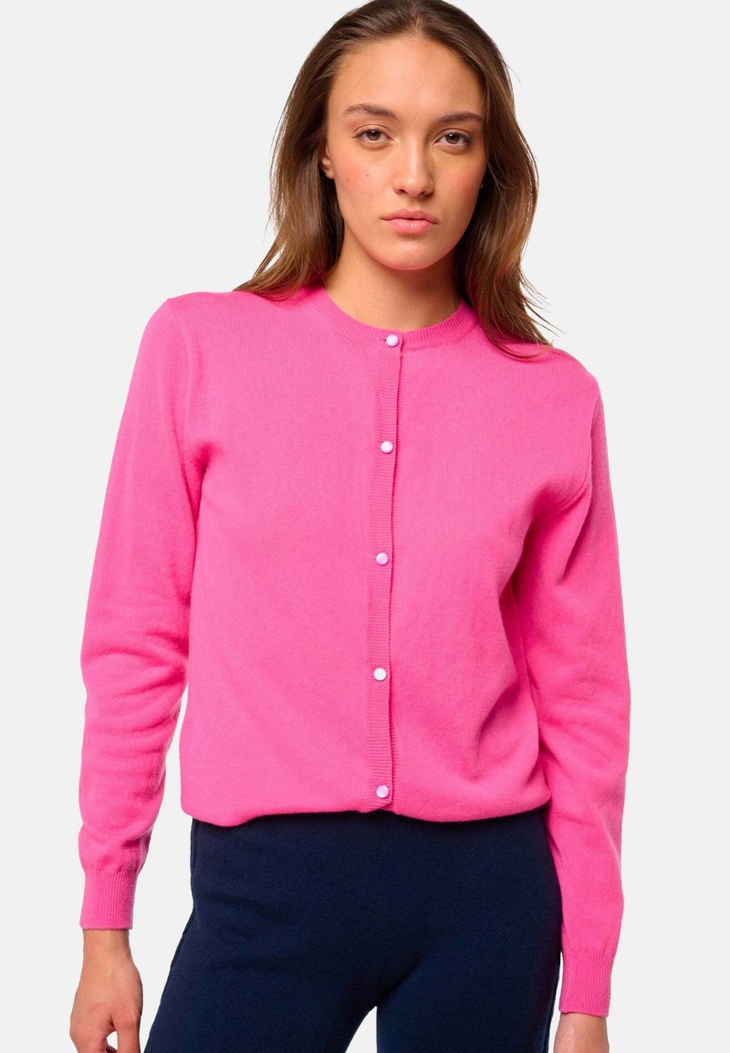 Cardigan rose vif en tissu doux avec un col rond et des boutons sur le devant. Il possède des manches longues et une silhouette ajustée.