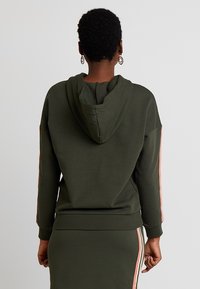 Olijfgroene hoodie met een relaxed fit, voorzien van roze zijstrepen. Gemaakt van zachte stof met ribgebreide mouwen en onderkant.