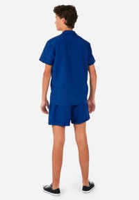 Blauwe short-sleeve shirt en bijpassende shorts gemaakt van lichte stof, met een relaxte pasvorm en eenvoudig ontwerp, gecombineerd met zwarte sneakers.