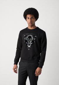 Sudadera negra con un gráfico de la cabeza de un feroz puma con ojos verdes, en un diseño triangular, hecha de una suave mezcla de algodón.