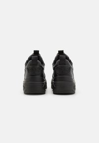 Sorte sneakers med en teksturert lærfinish, forsterket hæl og fremtredende logo på baksiden. Har en tykk såle og trekkflik.