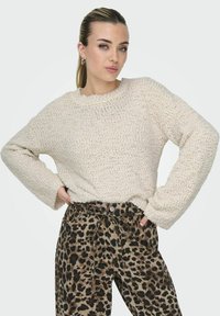 Maglione cremoso a trama con scollo rotondo e maniche lunghe, abbinato a pantaloni marrone con stampa leopardata e vita con cintura.