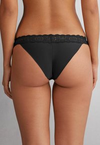 Zwarte stringonderbroek met een kant tailleband, voorzien van een gladde matte afwerking en een delicate bloemmotief op het kant.