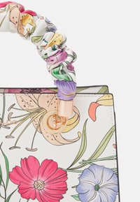 Floral handbag featuring a white textured exterior, colorful flower patterns, and a scrunchy handle in complementary colors with gold hardware.