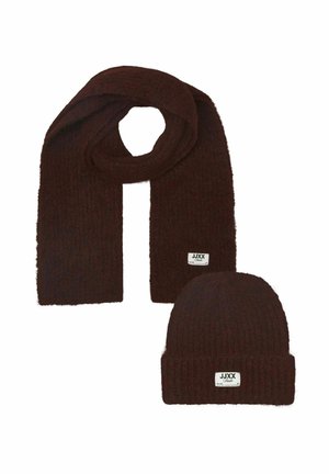 Conjunto de bufanda y gorro de punto de color marrón oscuro con pequeñas etiquetas blancas con la marca JJXX sobre un fondo blanco.