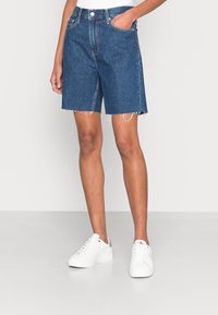 Jeansshorts, hög midja, mörkblå, rå nederkant, rak skärning, med framfickor, kombinerade med vita sneakers, minimalistisk design.