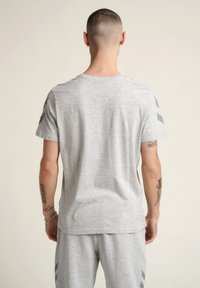 Szara koszulka z krótkim rękawem o okrągłym dekolcie. Miękka tkanina, gładka faktura, z ciemnoszarymi paskami akcentującymi na ramionach. Casualowy fason.