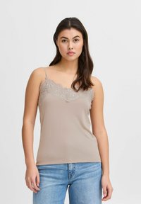 Top de tirantes color beige con cuello de encaje, tirantes finos ajustables y textura suave, combinado con jeans de mezclilla azul claro.