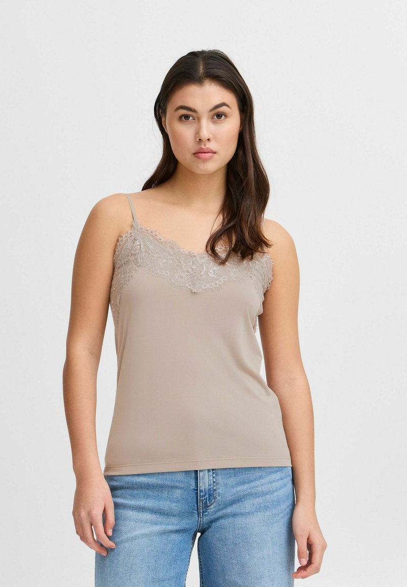 Top de tirantes color beige con cuello de encaje, tirantes finos ajustables y textura suave, combinado con jeans de mezclilla azul claro.