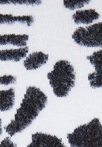 Tessuto a motivi in bianco e nero con una texture fuzzy che presenta forme irregolari su uno sfondo liscio. Il design include macchie contrastanti.