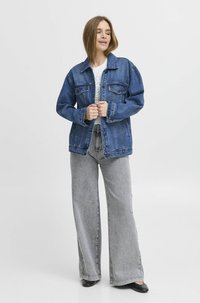 Jeans jakna u tamnoplavoj boji s klasičnim krojem, prednjim džepovima i kopčanjem na dugmadi, u kombinaciji sa svijetlosivim širokim trapericama.