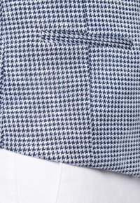 Niebiesko-białe tkanina w wzór houndstooth o gładkiej fakturze, z boczną kieszenią i dopasowanym krojem.