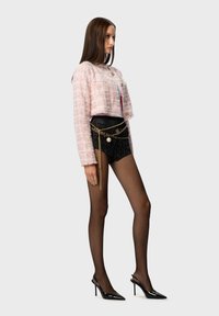 Pink tweed cropped jacket with frayed edges, paired with black shorts featuring chain accents. Model wears sheer black tights and pointed heels.