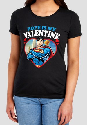 Woman wearing black shirt with Superman graphic inside a heart and text "Hope is my Valentine" above it.