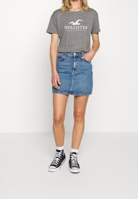 Grå bomulls-T-shirt med en rosa logotyp, kombinerad med en ljusblå denimkjol och svarta högskor med vita snörningar och strumpor.