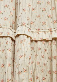 Tejido con estampado floral en crema, con delicadas flores en tonos rosa y amarillo. Texturizado con acentos plisados y detalles de volantes.