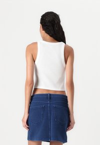 White ribbed crop top with wide straps, paired with a dark denim mini skirt featuring two back pockets and a smooth texture.