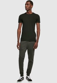 Zwarte katoenen t-shirt gecombineerd met donkergrijze joggingsbroek met getextureerde panelen en zwart-witte sneakers. Effen achtergrond.