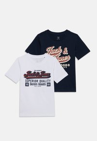 Zwei T-Shirts: eines weiß mit rot-blauer Druckgestaltung und eines navyfarben mit creme-rotem Druck, beide mit klassischem Rundhalsausschnitt und kurzen Ärmeln.