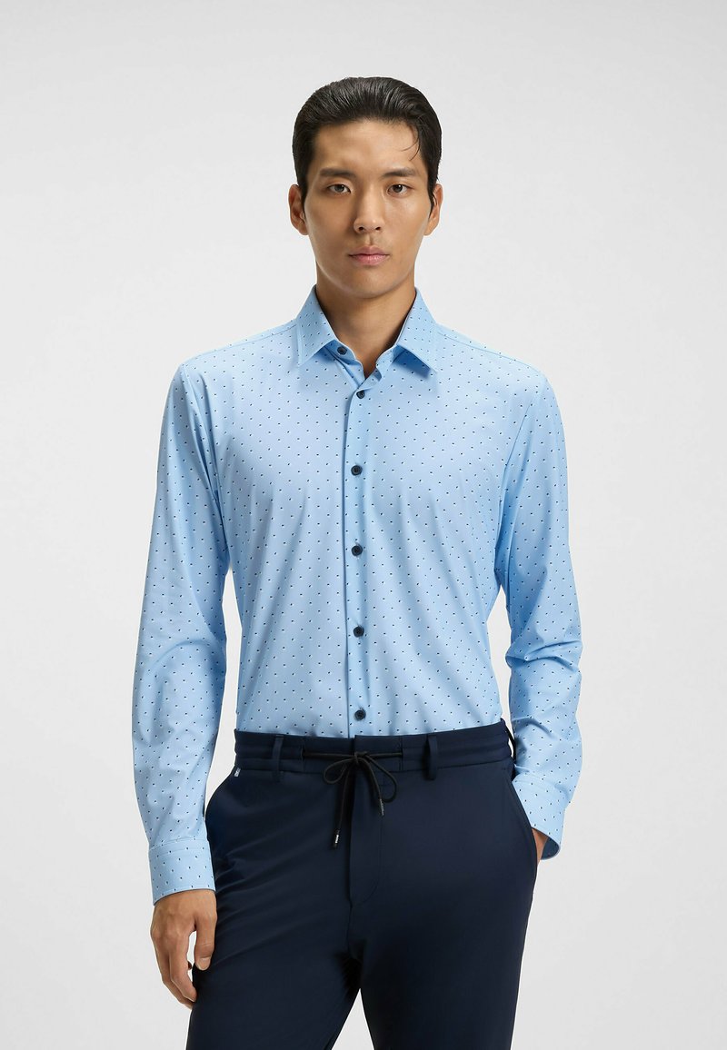 Camicia button-up azzurro chiaro con piccoli pois neri, maniche lunghe, colletto e bottoni neri. Indossata con pantaloni scuri.