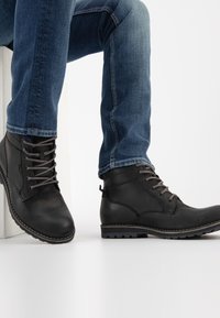 Black leather ankle boots with gray laces, round toes, and textured surfaces. Rubber soles with visible tread patterns. Jeans visible above.