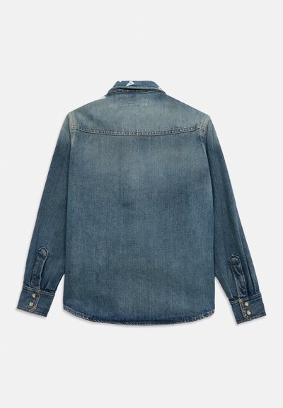 Πλάτη μπλε πουκαμίσου από τζιν με μακριά μανίκια, με κουμπωτές μανσέτες και γιακά, σε λευκό φόντο.