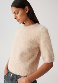 Helle rosa, flauschige Pullover mit Rundhalsausschnitt, kurzen Ärmeln und einem weichen, strukturierten Stoff, kombiniert mit dunkelgrauen Jeans.