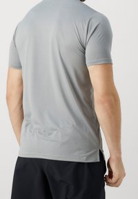 Camisa atlética gris de manga corta hecha de un tejido suave y ligero con una textura sutil y aberturas laterales para mayor movilidad.