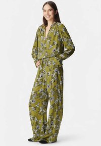Zielony kombinezon w kwiaty z długimi, bufkami rękawami i głębokim dekoltem w kształcie litery V. Wzór obejmuje czarno-białe kwiaty. Luźny, szerokie nogawki z szerokim krojem.