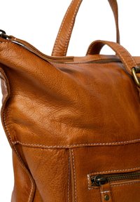 Bruine leren handtas met een gestructureerd oppervlak, voorzien van een ritsvak, versterkte stiksels en een stevige handgreep.