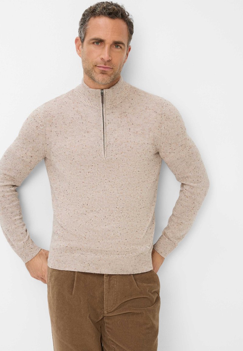Helles beige Pullover mit hohem Kragen, Frontreißverschluss und gesprenkelter Textur, kombiniert mit braunen Cordhosen.