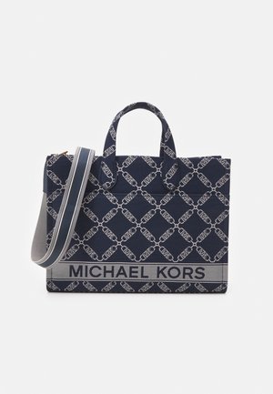 Sac cabas Michael Kors bleu marine et blanc avec motif chaîne, deux poignées supérieures et une large bandoulière réglable.
