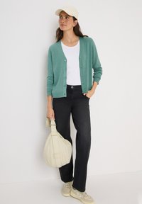 Ljusgrön cardigan med knäppning framtill, bärs över en vit t-shirt och svarta byxor. Beige keps och en krämfärgad hobo-väska fulländar outfiten.