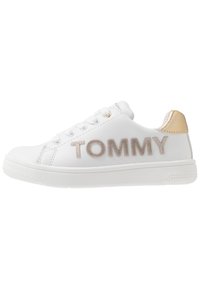 Zapatillas de cuero blancas con letras brillantes en beige "TOMMY" y detalles metálicos dorados en el talón. Diseño clásico con cordones y suela de goma.