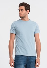 Lys blå kortærmet t-shirt med rund halsudskæring, glat tekstur og et diskret logomærke på den nederste side, iført med blå jeans.