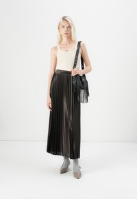 Jupe maxi plissée noire, finition satinée, associée à un débardeur crème à rayures. Accessoire inclut un sac à main noir avec des accents à franges.