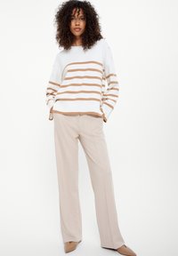 Maglione a righe in bianco e beige, con orlo a coste, abbinato a pantaloni beige a gamba larga e scarpe con punta.